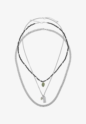 Tre collane a strati: una catena spessa in argento, una catena di perline nere con pietra verde e una catena sottile in argento con due piccoli pendenti in argento.