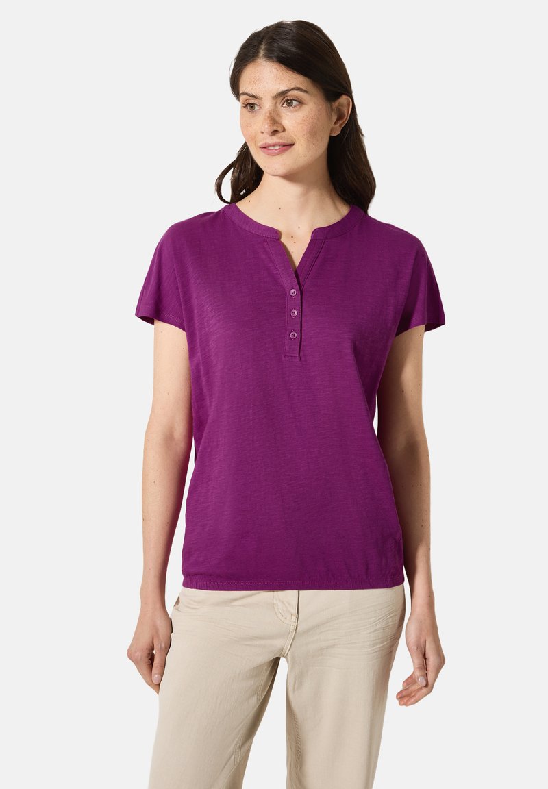 Top viola a maniche corte con scollatura henley e tre bottoni. Realizzato in tessuto morbido, presenta una vestibilità rilassata e una texture liscia.