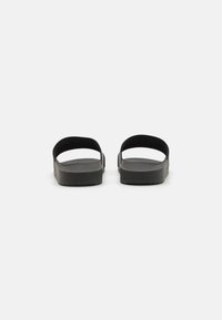 Sandale negre cu talpă plată, două curele late și un buclă pentru călcâi. Tălpică texturată și design minimalist fără elemente decorative suplimentare.
