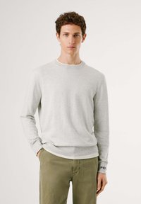 Suéter de cuello redondo gris claro, hecho de un material suave, con mangas largas y puños y dobladillo acanalados, con un sutil detalle de logo en el puño.