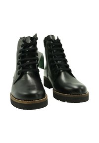 Botines de cuero negro con suelas gruesas negras, cordones negros, cremalleras laterales y un borde marrón, mostrados de frente sobre un fondo blanco.