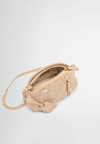 Quilted beiger Handtasche mit goldenen Beschlägen, Reißverschluss oben und Kettenriemen. Enthält ein Etikett mit Markenname und Logodetails.