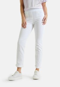 Weiße, enganliegende Jeans aus Denim mit hoher Taille und umgeschlagenen Säumen, kombiniert mit weißen Sneakers. Glatte Textur und keine sichtbaren Muster.