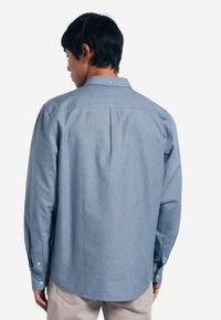 Camicia a maniche lunghe blu chiaro realizzata in tessuto morbido, con una piega sulla schiena, colletto abbottonato e polsini con bottoni.