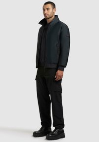 Svart bomberjakke med glidelås foran, ribbestrikkede mansjetter og sidelommer. Stilfullt kombinert med svarte cargobukser og kraftige svarte støvler.