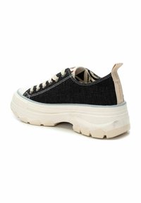 Zapatilla de tela negra con suela blanca gruesa, cordones crema y patrón texturizado. Incluye un bucle de tela en el talón para facilitar su uso.