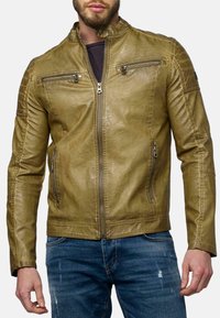 Giacca in pelle verde oliva con colletto rialzato, due tasche sul petto con zip e tasche laterali; presenta una finitura testurizzata e un design aderente.