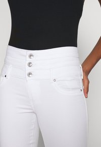 Jeans blancos de cintura alta con una textura suave, que presentan tres botones metálicos y un diseño tradicional de cinco bolsillos.