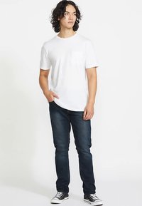 Biały bawełniany T-shirt z okrągłym dekoltem i krótkimi rękawami, zestawiony z ciemnoniebieskimi jeansami i czarnymi trampkami. Prosty wzór.