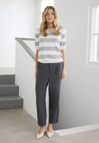 Sivo-bela črtasta majica s kratkimi rokavi, kombinirana s temno sivimi krojenimi hlačami in svetlo bež čevlji z okvirjenim koničastim prstom, na minimalističnem ozadju.