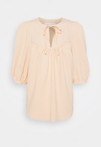 Blouse de couleur pêche en tissu doux, avec un col rond agrémenté d'un lien, des manches bouffantes et des détails froncés sur le devant.