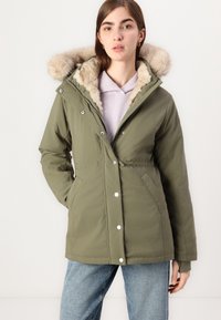 Olive roheline parka jakk faux karvase voodriga kapuutsiga, nööbikinnitusega, küljetaskute ja elastse vöökohtadega ning kena lõikega. Kantud kerge kampsuni üle.