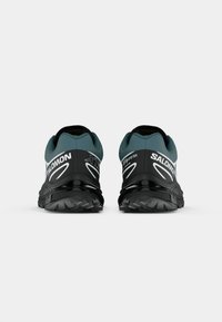 Zwarte en teal trailrunning schoenen met een Gore-Tex bovenwerk, een gestructureerde zool en opvallende witte branding. Lichtgewicht en duurzame constructie.