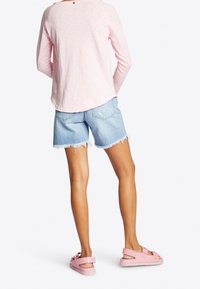 Hellrosa Langarmshirt, blaue Denim-Shorts mit fransigem Saum und blassrosa Sandalen mit Schnallen-Detail. Einfaches, lässiges Outfit.