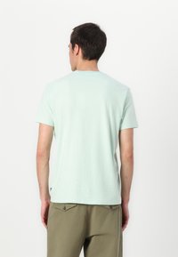 Camiseta de algodón en verde menta con cuello redondo y mangas cortas, con corte recto y un pequeño detalle de logo en la parte inferior izquierda.