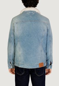 Giacca di denim blu sbiadito con colletto in shearling bianco, chiusura con bottoni e una toppa marrone del marchio vicino all'orlo. Presenta spacchi laterali.