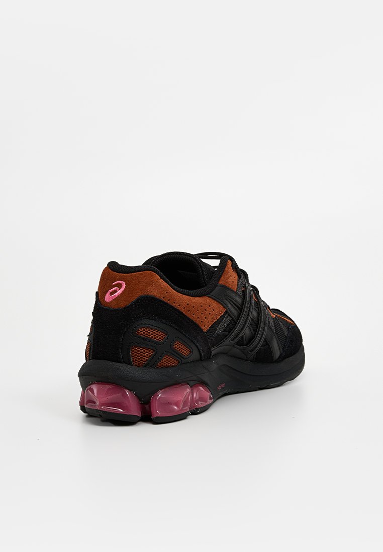 Scarpa sportiva nera e arancione con texture in rete e camoscio, dotata di un logo rosa ben in evidenza e di una suola nera e rosa, cuscinetta e bombata.