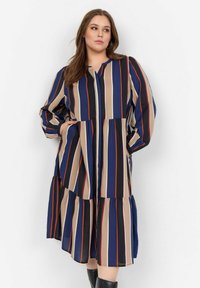 Robe rayée avec diverses couleurs incluant le bleu marine, le beige et le rouge ; coupe ample avec un ourlet à volants et des manches longues.