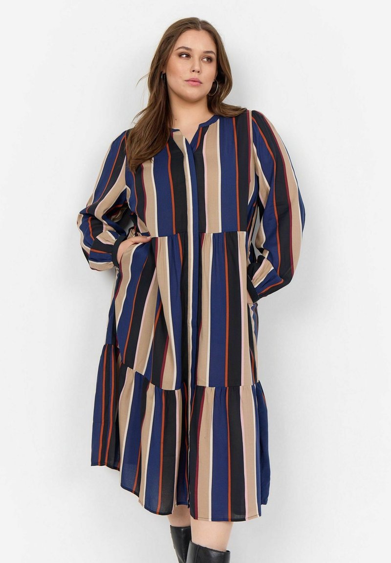 Robe rayée avec diverses couleurs incluant le bleu marine, le beige et le rouge ; coupe ample avec un ourlet à volants et des manches longues.