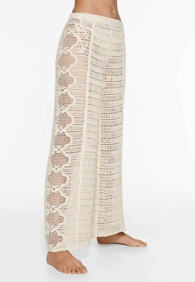 Pantalons larges en crochet crème avec des motifs ajourés et des accents en scallop sur les côtés.