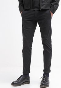 Svarta bomullsbukser med slim fit och uppvikta benslut, kombinerat med svarta läderskor med wingtip-detaljer.