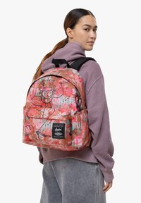 Ryggsäck med ett livfullt mönster i rosa och orange, accentuerat med graffiti-stil. Tillverkad av tyg med en stor framficka och justerbara remmar.