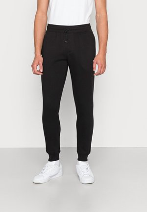 Black sweatpants made of soft fabric, featuring a drawstring waist, tapered legs, and ribbed cuffs, paired with white sneakers.