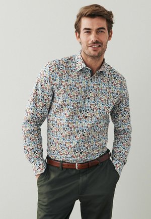 Cămașă albă cu guler, cu un model floral colorat, având nuanțe de albastru, roșu și verde. Purtați-o cu pantaloni închisi la culoare și o curea maro.