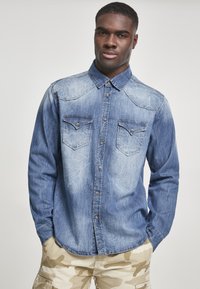 Denim košulja svijetloplave boje s dugim rukavima, prednjim dugmadi, dva džepa na prsima i suptilnim izbljeđivanjem. Izgleda ležerno i udobno.