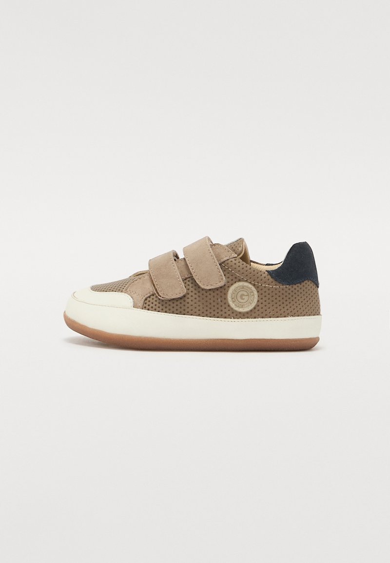 Zapatos infantiles en tonos marrón claro y azul oscuro, con cuero ante perforado, suela de goma blanca y correas de Velcro; detalle de logo circular en el costado.