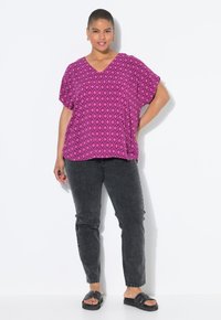 Top rosa a fantasia con scollo a V e maniche larghe, abbinato a jeans grigio scuro e sandali neri. Tessuto morbido e leggero.