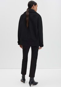 Giacca nera in misto lana con colletto ampio, vestibilità comoda e polsini con bottoni, abbinata a pantaloni neri slim e stivaletti.