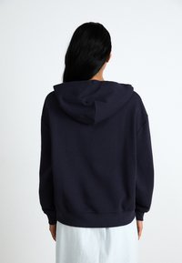 Navy blue hoodie with a drawstring hood, dropped shoulders, and ribbed cuffs. Soft material with a smooth texture, no visible patterns.