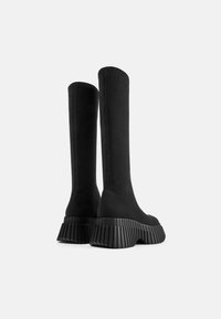 Botas de tobillo de punto negro con un caña alta y suela de plataforma gruesa y texturizada con estrías verticales para mayor tracción.