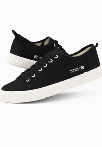 Sneaker neri in canvas con suole in gomma bianca, caratterizzati da una superficie liscia, punta rotonda, design con lacci e un'etichetta stampata sul lato.