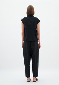 Black short-sleeved top with a high neck and smooth texture, paired with loose black trousers, viewed from the back against a white background.