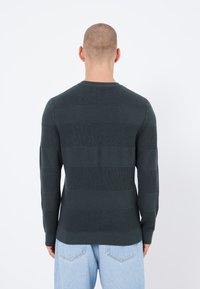 Pull en maille vert foncé avec des rayures horizontales côtelées. Avec un col rond et des manches longues, associé à un jean bleu clair.