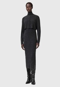 Harmaa neulottu kaksiosainen asu, jossa on lyhyt, korkeakauluksinen neulepusero nappidetaljilla ja pitkä, vartalonmyötäinen hame sivuhalkiolla.