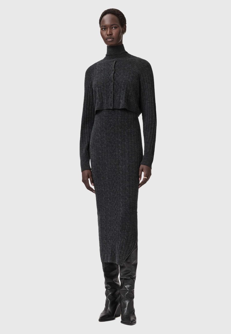 Harmaa neulottu kaksiosainen asu, jossa on lyhyt, korkeakauluksinen neulepusero nappidetaljilla ja pitkä, vartalonmyötäinen hame sivuhalkiolla.