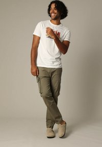 Witte katoenen T-shirt met grafisch ontwerp, olijfgroene cargobroek met zijzakken en beige instap-schoenen.