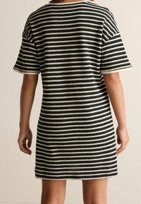 Robe rayée présentant des couleurs alternées noir et crème, manches courtes et coupe ample. Le tissu a une apparence tricotée texturée.