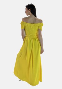 Off-the-shoulder gul maxi-kjole med smocket bodice, korte pufærmer og blødt skørt lavet af letvægtigt stof.