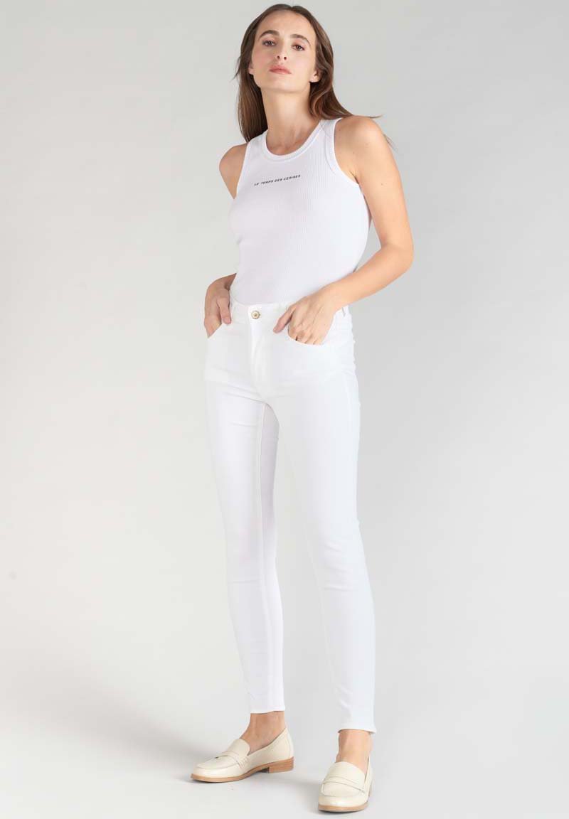 Witte geribbelde tanktop met een ronde halslijn en zwarte tekst, gecombineerd met hoge witte skinny jeans en lichtgekleurde loafers.
