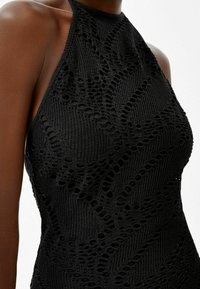 Haut noir à col halter en tissu tricot texturé avec des motifs ajourés et une silhouette ajustée, mettant en avant des détails de conception complexes.
