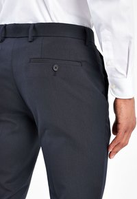Pantalones oscuros de color navy hechos de una tela suave, con un único bolsillo trasero con botón y un corte entallado con presillas para cinturón.