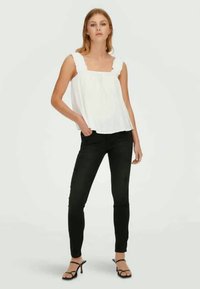 White sleeveless top with ruffled neckline, paired with slim black jeans and black strappy heels. Simple, clean lines and light fabric texture.