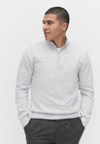 Jasnoszara bluza z zamkiem w miękkim materiale, z wysokim kołnierzem i ściągaczami, połączona z ciemnoszarymi spodniami.