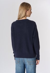 Maglione lavorato a maglia blu navy con vestibilità morbida, trama a coste e scollo tondo. Indossato con jeans denim azzurri chiari con tasche posteriori.
