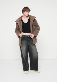Hnedá teddy bunda so širokým golierom, čierny crop top, svetlošedé široké nohavice a krémové tenisky. Textúrovaná tkanina; ležérny dizajn.