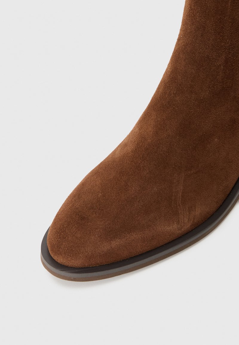 Braune Wildleder-Stiefelette mit spitzem Zehenbereich und schlankem Design, das eine dünne, dunkle Laufsohle aufweist. Die glatte Textur steht im Kontrast zu der satten Farbe.